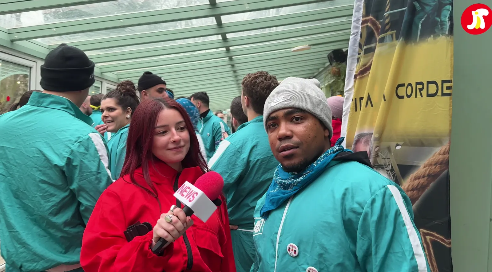 Une interview micro en main sur un événement, l'équipe en survêtement turquoise derrière